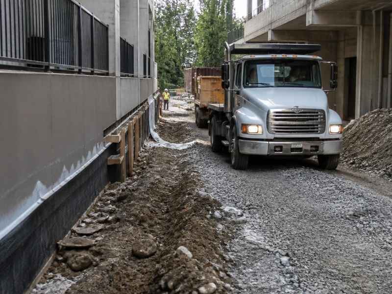 Dump truck using a narrow temporary construction access route between buildings in Knoxville, TN, during active site work.